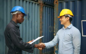 Terminal operators wearing hard hats in a terminal container yard are shaking hands
