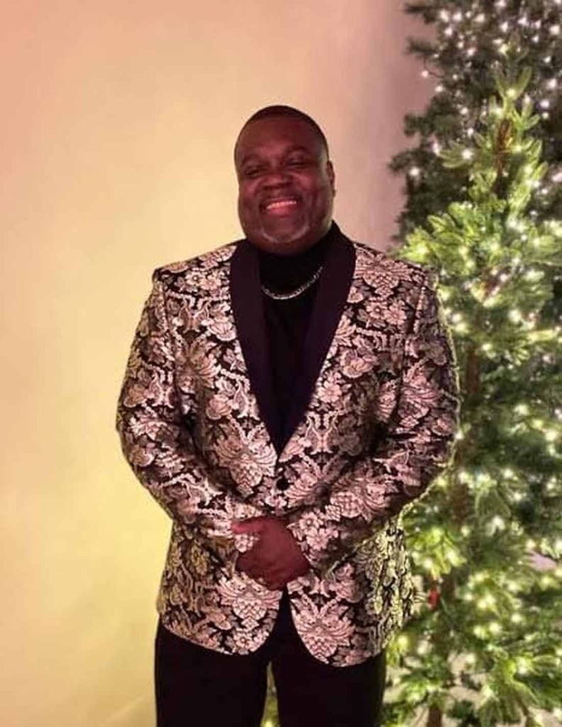 William McKinnon dressed up in a blazer posing for a photo next to a christmas tree